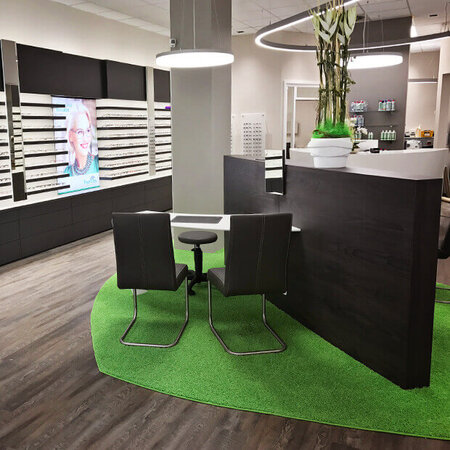 Modern eingerichtetes Optiker-Geschäft mit Beratungstisch, Brillenauswahl und Dekoration.